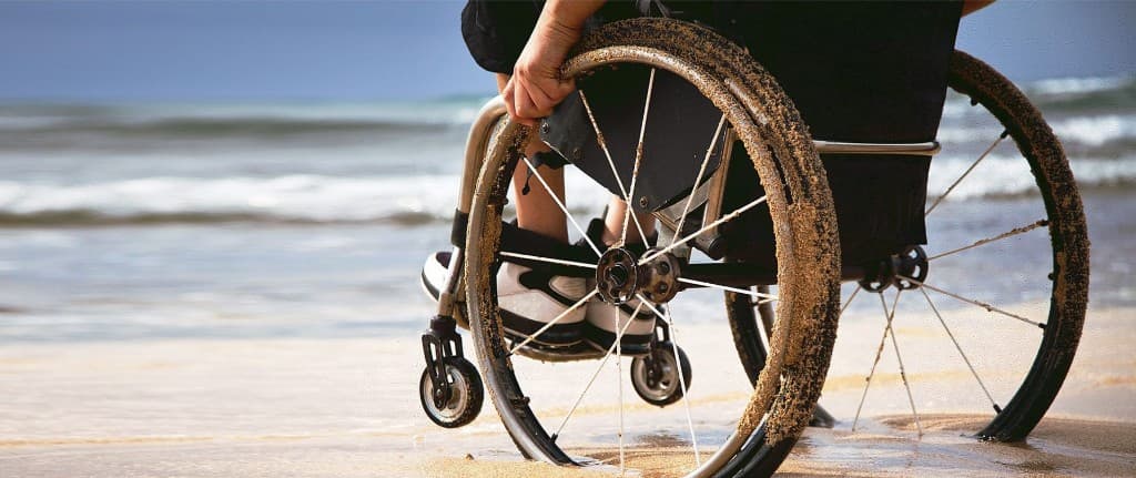 Person in a manual wheelchair on the beach, facing the ocean